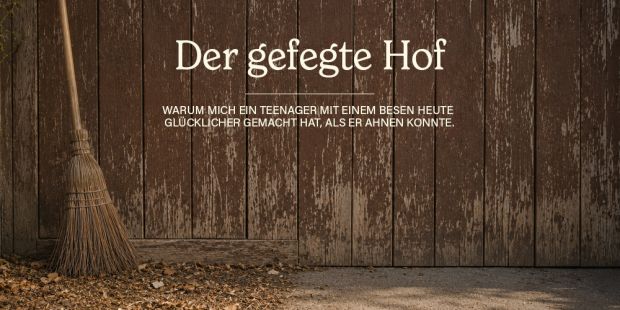 Ein Besen vor einem alten, braunen Scheunentor, der Boden ist auf einer Seite gefegt, auf der anderen Seite liegen vertrocknet Blätter.